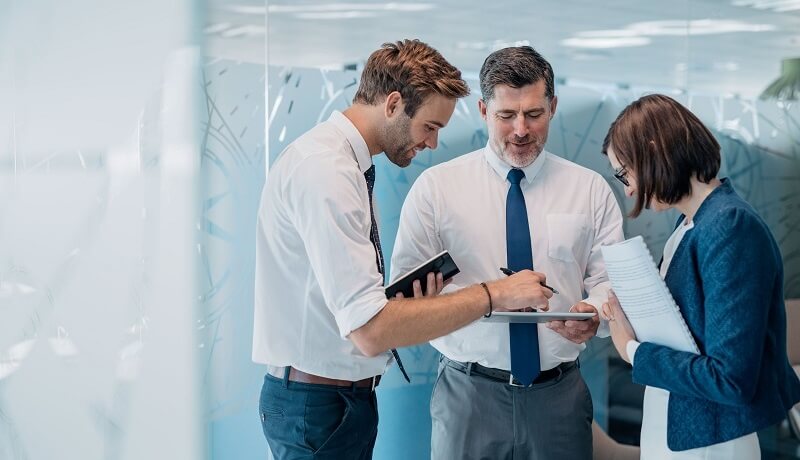 Drei Kollegen besprechen im Büro ein Dokument zur Finanzberatung und Planung